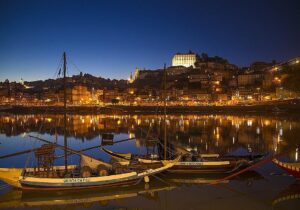 Photo nocturne du bateau traditionnel Rabelo, utilisé autrefois pour le transport des vins de la région du Douro, sur la rive de Vila Nova de Gaia, avec l'éclairage nocturne mettant en valeur le paysage pittoresque le long du Douro