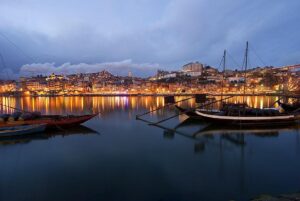 Photo nocturne du bateau traditionnel Rabelo, utilisé autrefois pour le transport des vins de la région du Douro, sur la rive de Vila Nova de Gaia, avec l'éclairage nocturne mettant en valeur le paysage pittoresque le long du Douro.